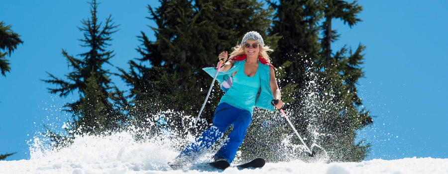 esquiadora bajando una pista en semana santa con la chaqueta abierta y sin guantes con la nieve primavera